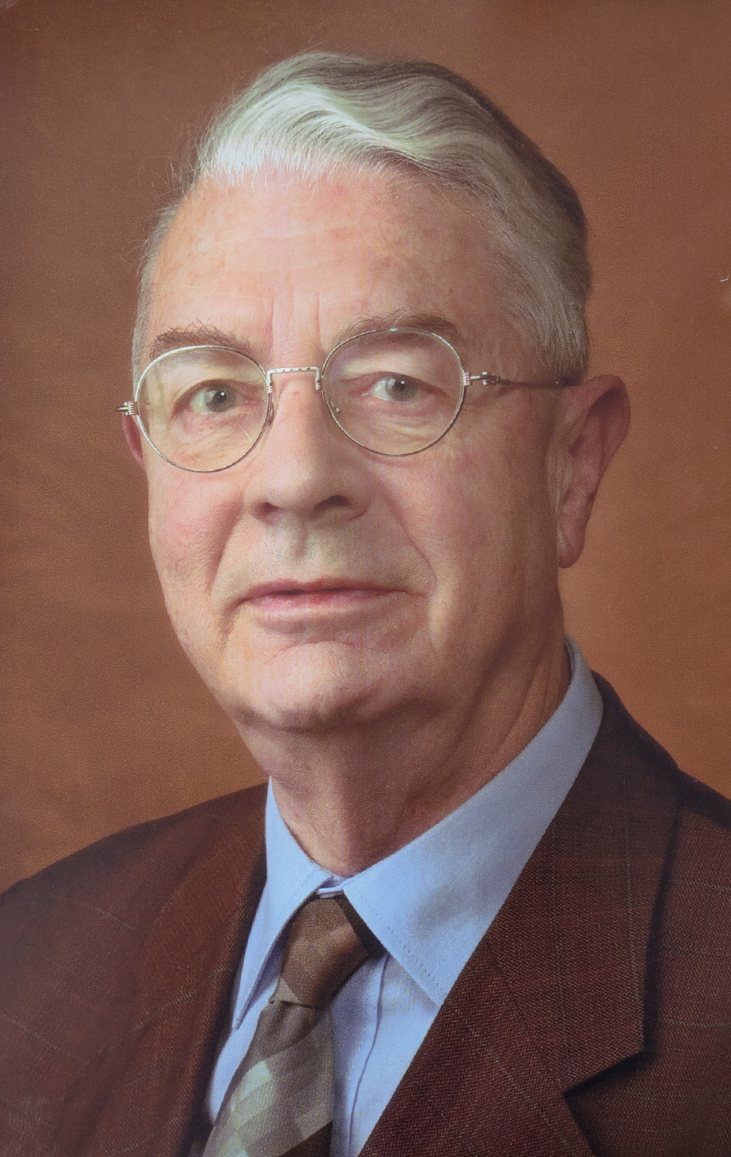 Ein Porträt eines älteren Herren mit Brille, weißen Haaren, fliehender Stirn im Anzug mit Krawatte auf braunem Hintergrund. Nikolaus Walter.